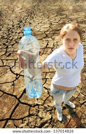 young girl in casual clothing standing in the desert on the cracked ground with outstretched an empty plastic bottle  idea of ??disaster and bad environment and pollution from emissions fresh water