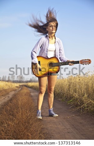 young beautiful girl jump with guitar outdoors on blue sky background