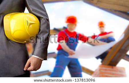 engineer yellow helmet for workers security on background of two construction workers are on the roof of the house with the construction plan in hand
