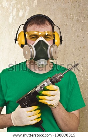 Worker with a drill in yellow protective glasses, ear plugs and respirator
