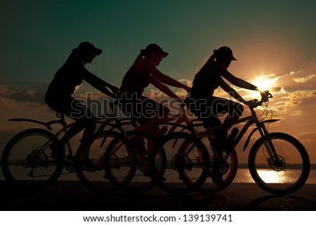 Image of sporty company friends on bicycles outdoors against sunset. Silhouette The three phases of motion of a single cyclist along the shoreline coast
