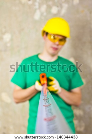 The builder measures the length of the tape measure on the background of a concrete wall