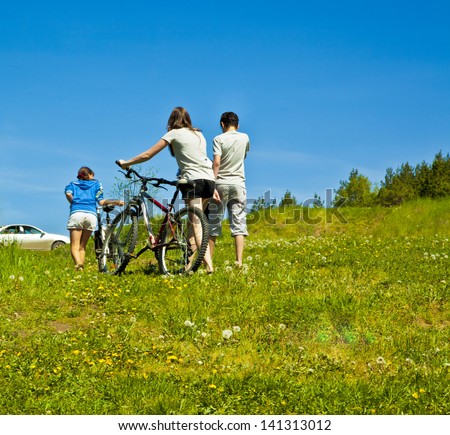 company of three teenagers goes backs after a walk to the car on a background summer lawn and blue sky
