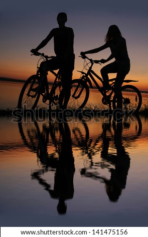 two mountain biker silhouette in sunrise with reflection in water