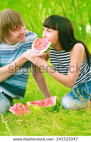 Young couple eating water melon. Pair with a watermelon couple on a picnic in the forest together bite a one piece of watermelon - a symbol of unity and oneness