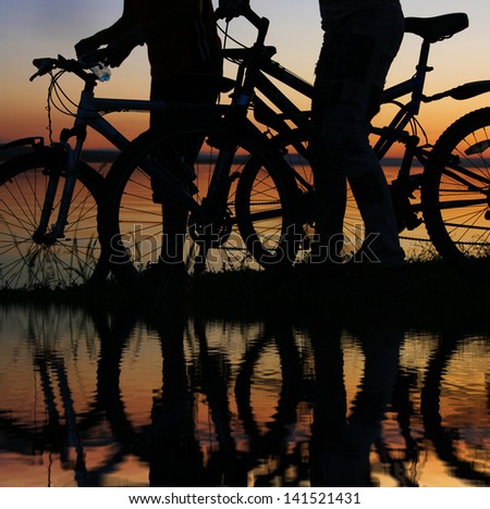 silhouettes of couples in love ride bicycles along the beach with reflection