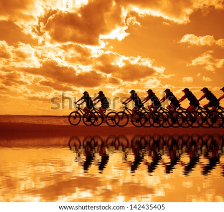 Image Of Sporty Company Friends On Bicycles Outdoors Against Sunset. Silhouette A Lot Phases Of Motion Of A Single Cyclist Along The Shoreline Coast Reflection On Water Space For Inscription