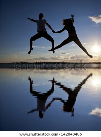 Silhouettes of couple jumping on blue sunset background with reflection
