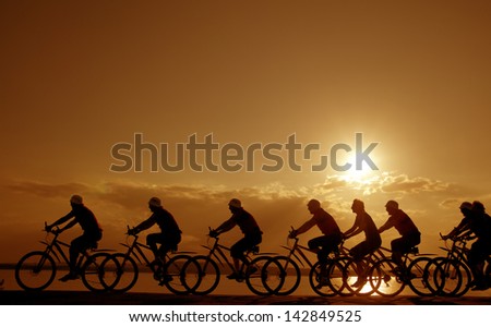 Image of sporty company friends on bicycles outdoors against sunset. Silhouette A lot phases of motion of a single cyclist along the shoreline coast