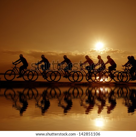 Image of sporty company friends on bicycles outdoors against sunset. Silhouette A lot phases of motion of a single cyclist along the shoreline coast Reflection on water Space for iscription