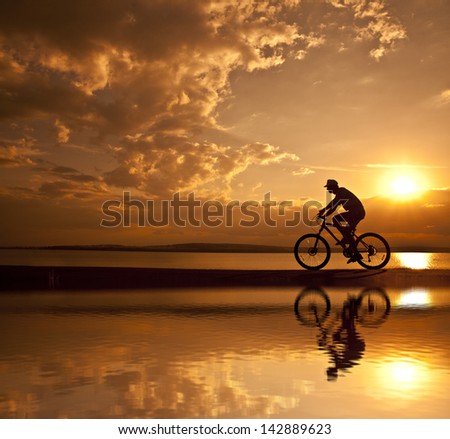 silhouette of a cyclist at sunset with a blurred reflection in the water with ripples