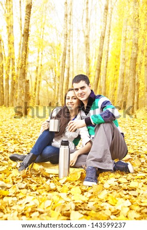 Young latin hispanic pair in yellow forest wood sitting on  leaves and drink hot coffee from a thermos heating copy Space for inscription