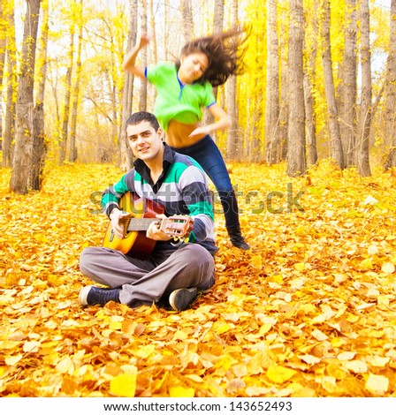 Woman jumping and dancing man sitting on a autumn forest with acoustic guitar Copy Space for inscription