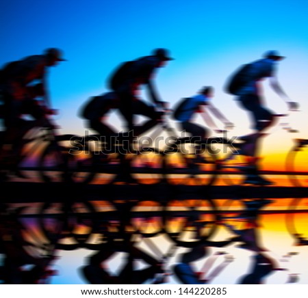 Image of sporty company friends on bicycles outdoors against sunset. Silhouette A lot phases of motion couple of cyclist along the shoreline coast With reflection on water