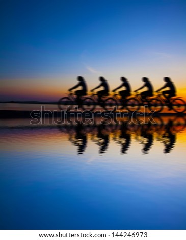 Blurred silhouette of people Image sporty company friends on bicycles outdoors against sunset Silhouette with reflection on water  A lot phases of motion of single cyclist along the shoreline coast