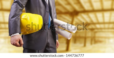 engineer yellow helmet for workers security with construction plans on background empty yellow warenhouse