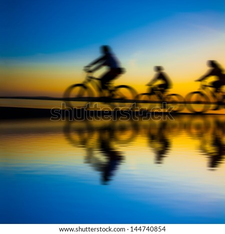 Blurred silhouette of people Image of sporty company friends on bicycles outdoors against sunset. Silhouette A lot phases of motion couple of cyclist along the shoreline coast