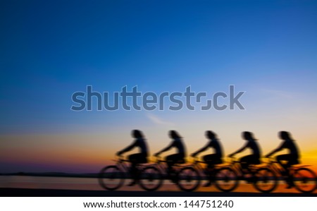 Blurred silhouette of people Image of sporty company friends on bicycles outdoors against sunset. Silhouette The four phases of motion of a single cyclist along the shoreline coast