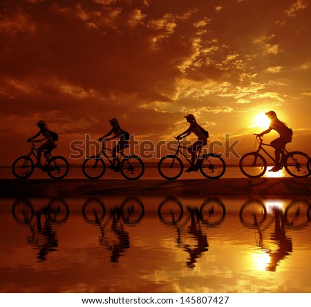 Image of four sporty company friends on bicycles outdoors against sunset. Silhouette A lot phases motion of a single cyclist along shoreline coast with reflection on water Copy space for inscription