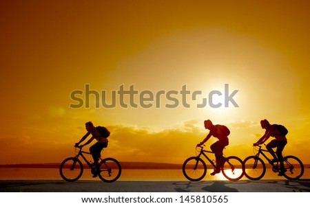 Image of sporty company friends on bicycles outdoors against sunset. Silhouette A lot phases of motion of a single cyclist along the shoreline coast  copy Space for inscription