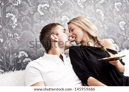 young caucasian couple sitting on a couch together a cookie bite her lips Copy space for inscription