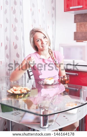 blondy girl holding a spoon with cake in pink t-shirt sitting in the kitchen Copy space for inscription