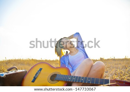 Country hippie girl with guitar at wheat field on the old retro suitcase Copy space for inscription