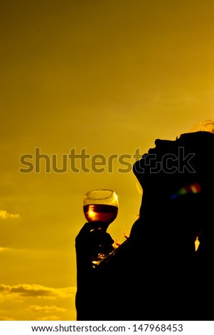 silhouette of a young woman in the background of the yellow sky with a glass of white wine Copy space for inscription