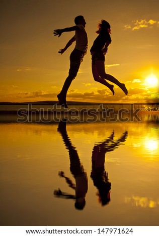 Silhouettes of couple jumping on sunset background Copy space for inscription With reflection on water