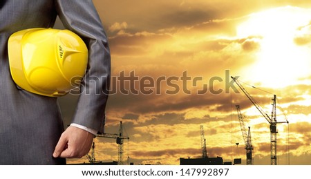 engineer yellow helmet for workers security on the background of a new high-rise apartment buildings and construction cranes and evening sunset sky Copy space for inscription  Horizontal