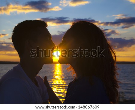 Silhouette of kissing couple over orange sunset background Sun between lips Copy space for inscription