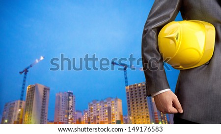 engineer yellow helmet for workers security on the background of a new high-rise apartment buildings and construction cranes and evening blue sunset sky