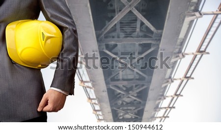 worker or engineer holding in hands yellow helmet for workers security on the background of a new concrete bridge over the river in perspective buildings gray idea building new road junctions