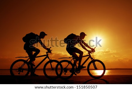 Image of sporty company couple - two friends on bicycles outdoors against sunset. Silhouette A lot phases of motion single cyclist along the shoreline coast Reflection on water Space for inscription
