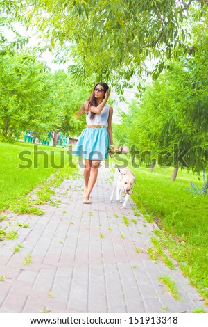 Young latin hispanic brunette Woman wear blue dress walking with white dog - labrador along the path laid paving stones Copy space for inscription