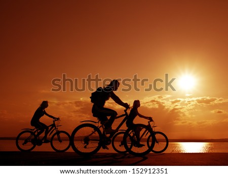 Image of sporty company three friends on bicycles outdoors against sunset. Silhouette A lot phases of motion of a single cyclist along the shoreline coast  Space for inscription