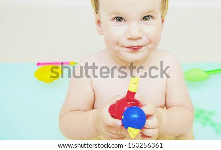 Little baby girl holding toy in hands bath with blue water at home Copy space for inscription