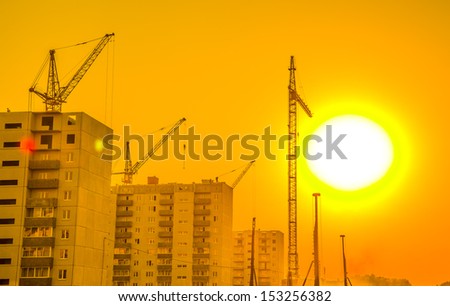 Hoisting crane and the contours of house under construction sunset view