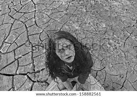 Young ginger woman alone in the darkness on dry craced desert view from the top White and black Copy space for inscription