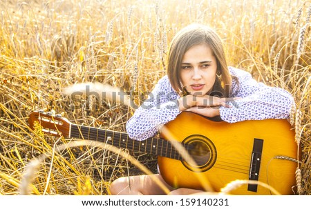 Country latin hispanic girl sitting and dreaming with guitar at golden wheat field Copy space for inscription