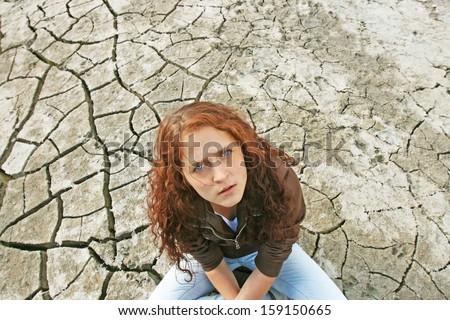 Young ginger woman alone in the darkness on dry cracked desert view from the top  Copy space for inscription