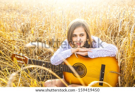 Country latin hispanic girl sitting and dreaming with guitar at sunset golden wheat field Copy space for inscription