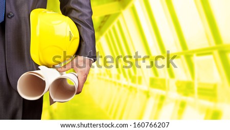 engineer yellow helmet for workers security with construction paper plans on the background of a new apartment buildings of glass