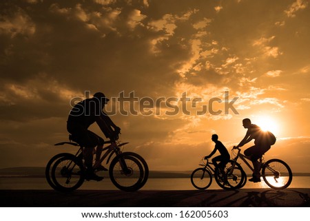 two romantic couples cyclists ride towards each other silhouette in sunrise   against sun set cloudy sky and sea shore background Space for inscription