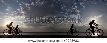 Image of sporty company friends on bicycles outdoors against sunset Silhouette with .  cyclist along the shoreline coast Space for inscription
