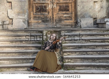 Young sexy with long hair with a broken violin on old retro fence  in the Gothic style of classicism