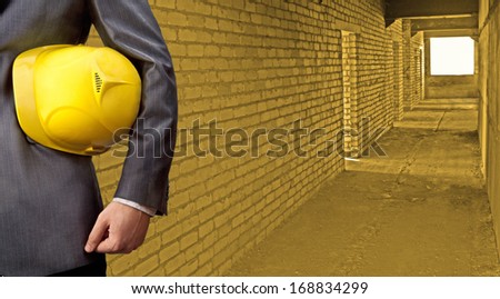 adult torso engineer or inspector hand holding yellow plastic helmet for workers security on the background of a new apartment buildings inside of yellow No face Copy space for inscription