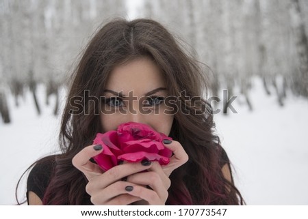 Close up portrait of Young adult latin hispanic brunette Girl in winter cold december forest hold red rose in black dress on brunch trees and white snow background