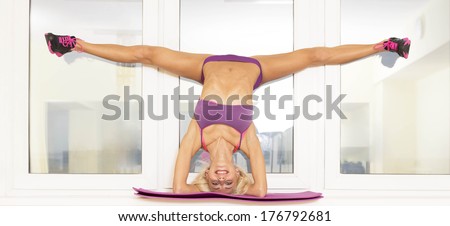 Portrait of young adult sexy girl with long blond hair in sexy clothes doing splits in air on windowsill leaning on his head hands is engaged in sports and yoga standing on glass  window background