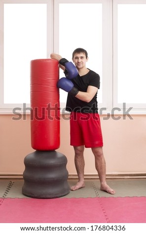 Portrait of young adult Boxer holding red punching bag standing on tatami on pink wall window background Asian man in red shorts black shirt in full length based on pear Copy space for inscription
